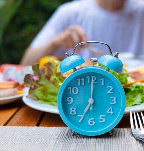 A clock and a healthy meal representing the intermittent fasting for fat loss schedule.